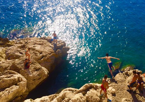A group of teenagers jumping off a cliff into the water below.