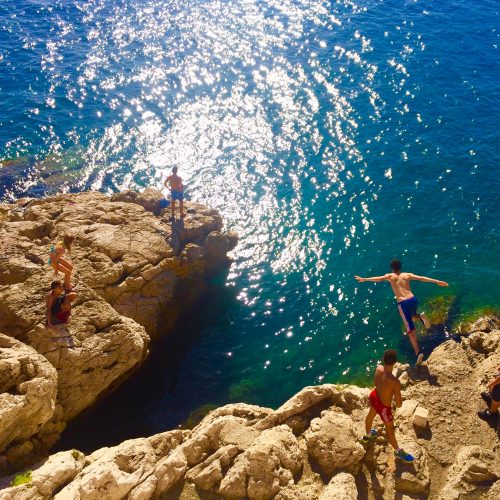 A group of teenagers jumping off a cliff into the water below.