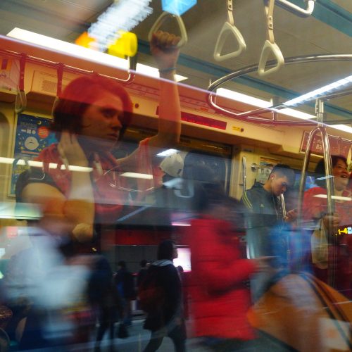 A picture through the window of a subway car showing the passengers inside and also reflecting the people walking on the platform outside.
