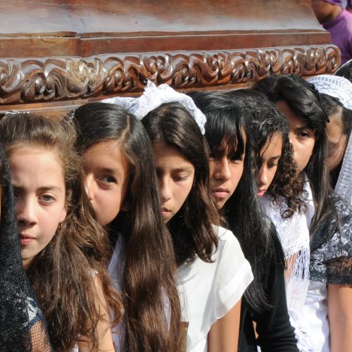 A line of young girls holding up a wooden parade float.