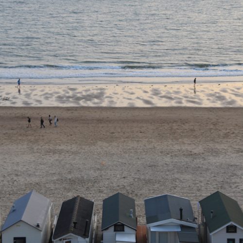 A line of tiny houses in front of a beach with a large shipping barge in the background.