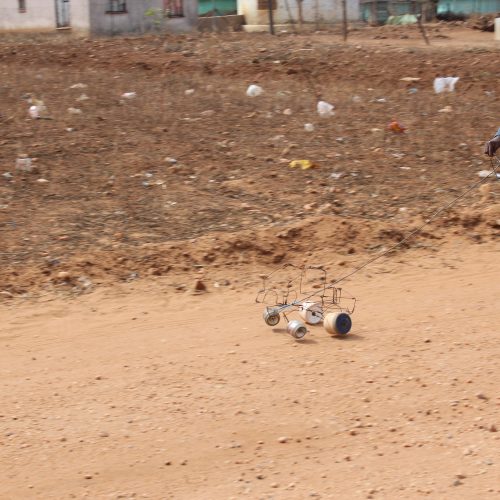 A boy running behind a toy car made of scrap.