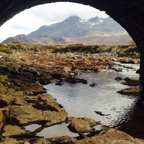 A river with mountains in the background, taken under a bridge so it looks as if there's a tunnel around the iamge.
