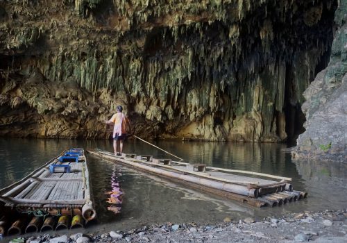 A man rowing a longboat into the entrance of a cave.