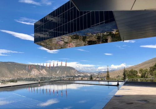 A picture of the UNASUR building with multiple flagpoles being reflected in a pool.